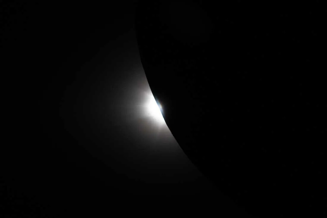 art002e009299 (April 6, 2026) – Captured from the Orion spacecraft near the end of the Artemis II lunar flyby on April 6, this image shows the Sun beginning to peek out from behind the Moon as the eclipse transitions out of totality. Only a portion of the Moon is visible in frame, its curved edge revealing a bright sliver of sunlight returning after nearly an hour of darkness. In final moments of the eclipse observed by the crew, the reemerging light creates a sharp contrast against the Moon’s silhouette and reveals lunar topography not usually visible along the lunar limb. This fleeting phase captures the dynamic alignment of the Sun, Moon, and spacecraft as Orion continues its journey back from the far side of the Moon.
