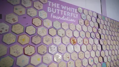 A wall of cream ceramic tiles on a purple wall.