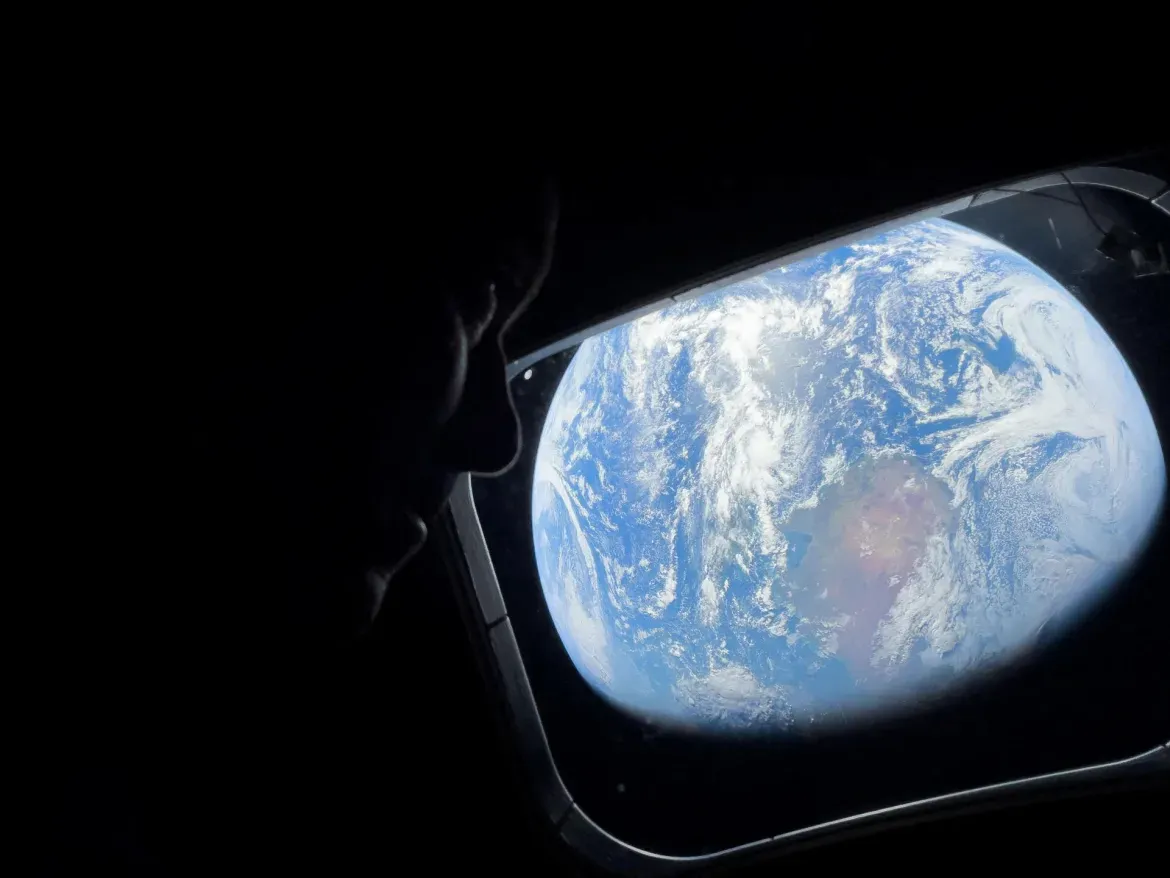 Artemis II Commander Reid Wiseman peers out of one of the Orion spacecraft's main cabin windows for a look back at Earth.