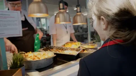 School student is being served by dinner lady in canteen.