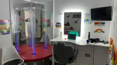 A sensory room featuring chairs, an Ipad, a mirror and toys.