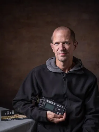 A man holds an ultrasound detector and rests his arm on a book