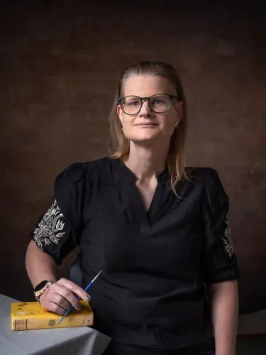 A woman holds a small brush and rests her hand on a book