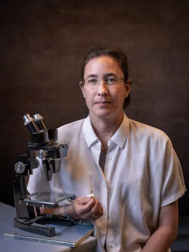 A woman poses next to a microscope and a book