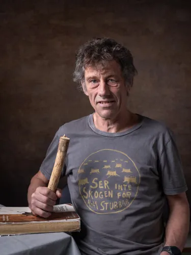 A man holds a wooden stick that rests on a book