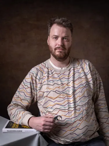 A man holds a pocket magnifying glass and rests his arm on a book