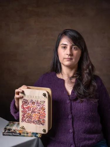 A woman holds up a herbarium that rests on a book