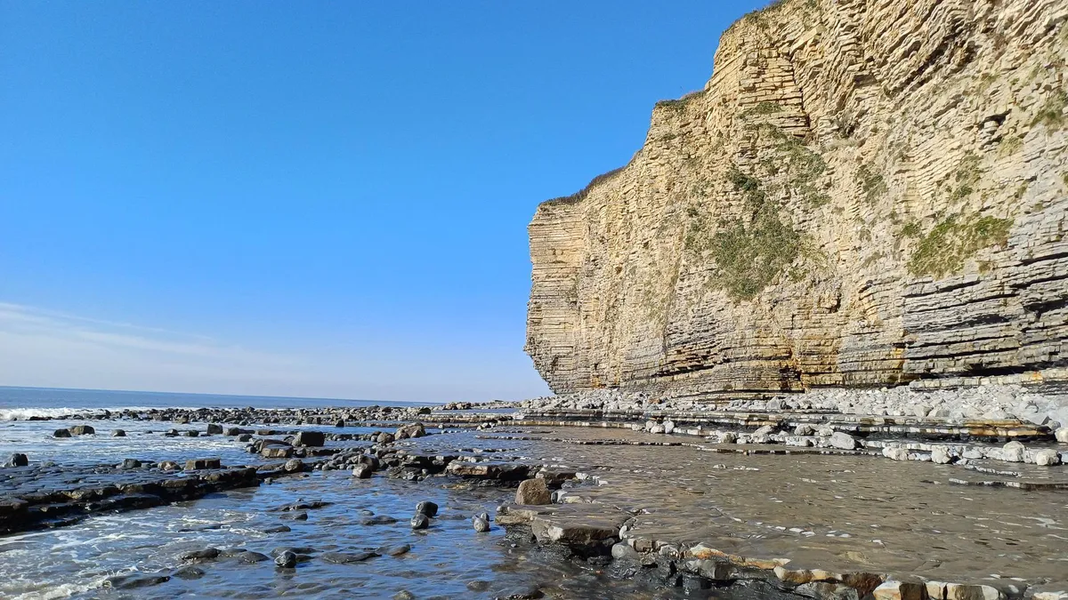 a tall limestone cliff above the sea on a blue sky day
