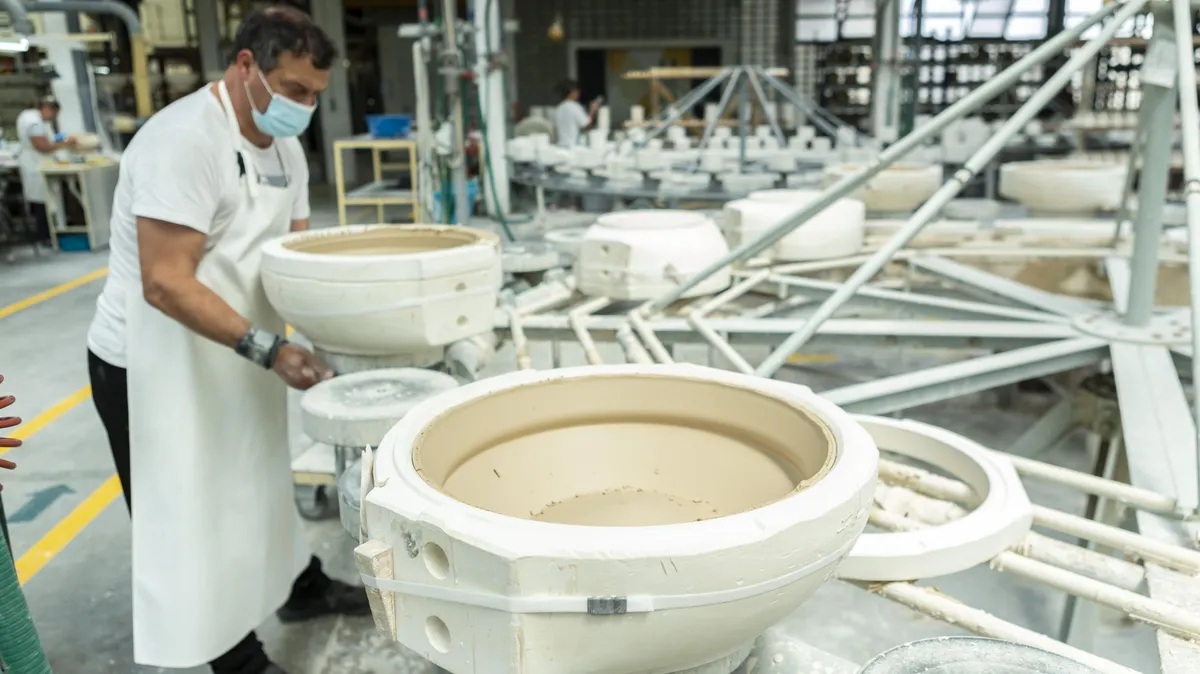 A worker stands on a production line of large porcelain bowls.