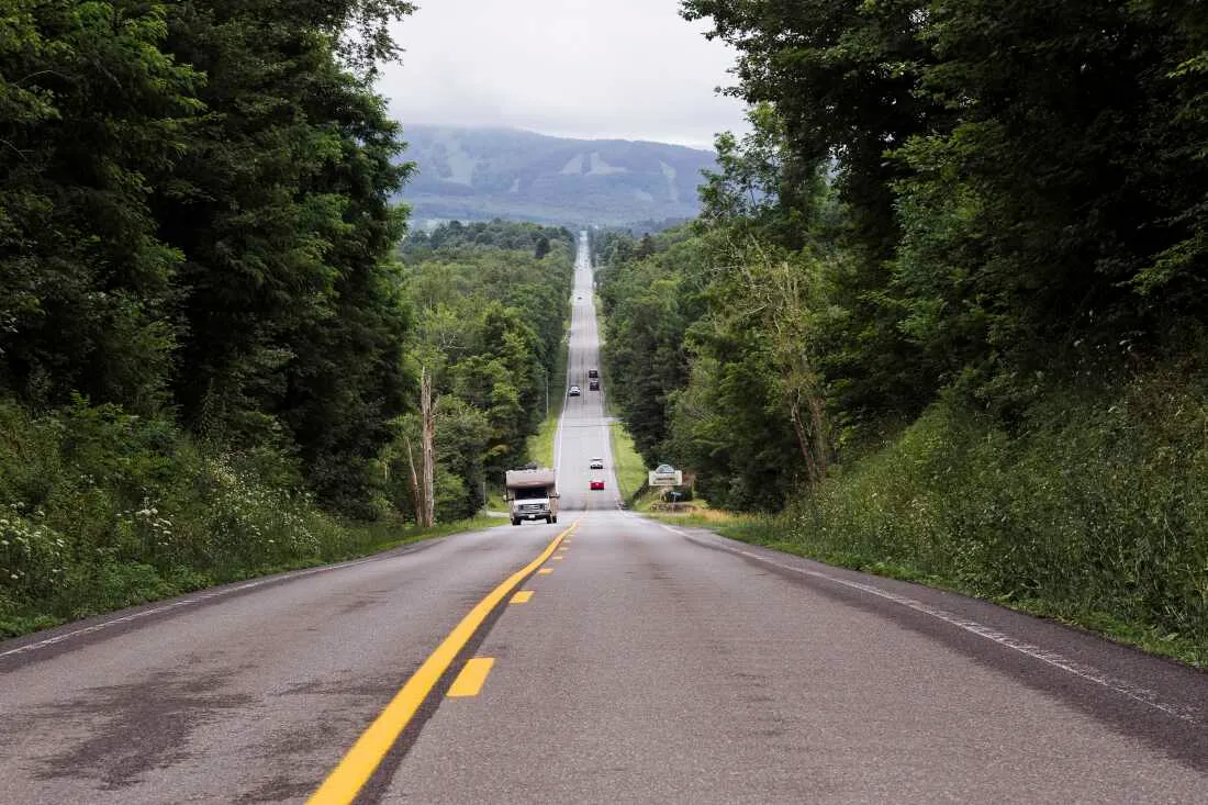 A two-lane road stretches downhill into the distance with trees on both sides.