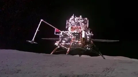 The Chinese lander-ascender mooncraft is pictured while being captured from the 'mobile camera' carried by the Chang'e-6 probe (out of frame), as it holds out a Chinese flag while stood on the surface of the moon against the dark abyss of space during China's moon mission on 4 June, 2024.