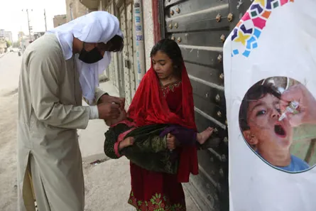 A health worker bends over a child who is being held by an older child.