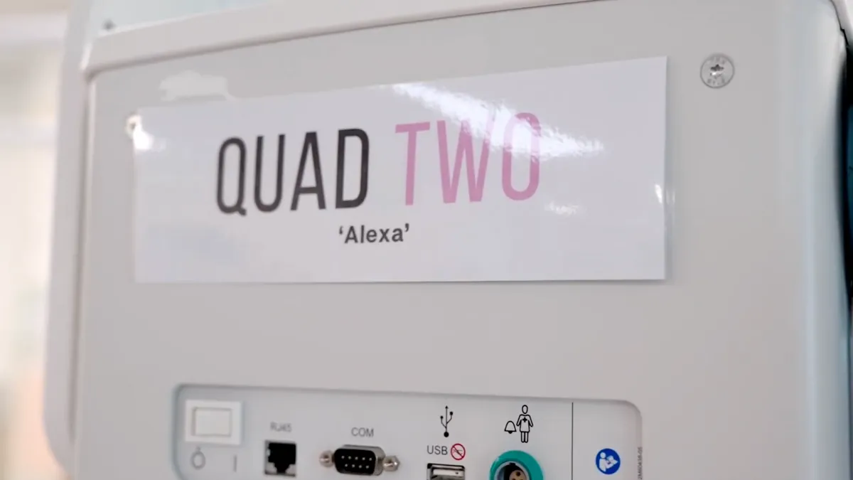 The side of a baby incubator with a laminated sign attached to it that reads 'Quad Two 'Alexa''