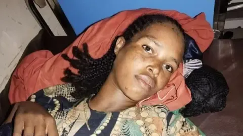Close-up of Bedriya lying down. She is wearing a printed green and black top and is resting her head on a red blanket