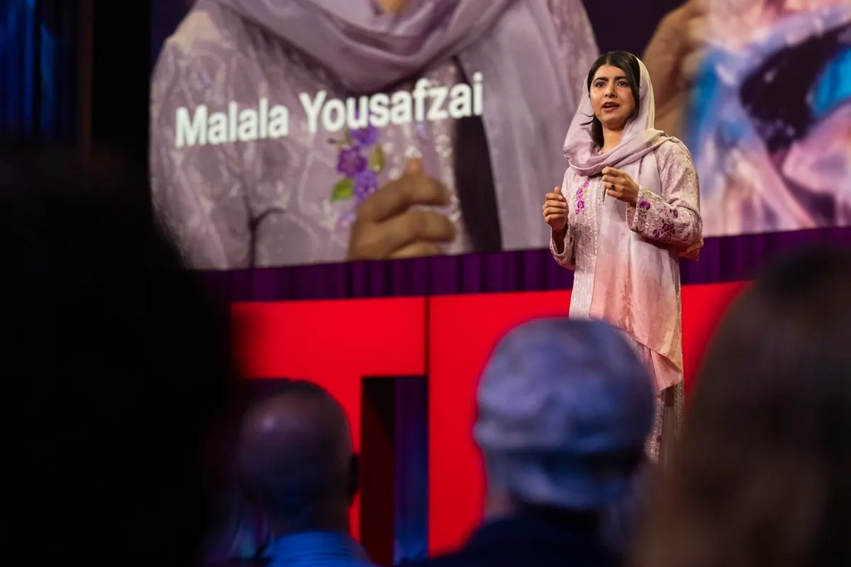 Malala, dressed in pink, stands on stage for TED Talk