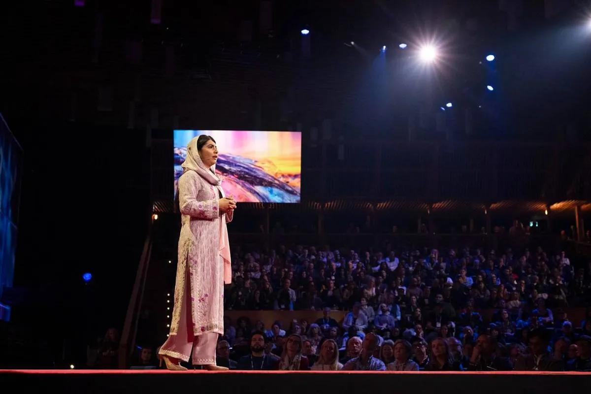 Malala, dressed in pink, stands on stage for TED Talk
