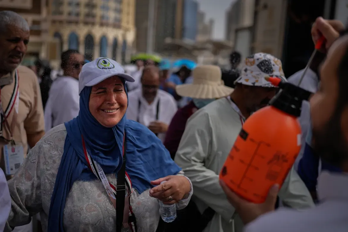 A Muslim pilgrim reacts as a volunteer sprays water to help her cool off.