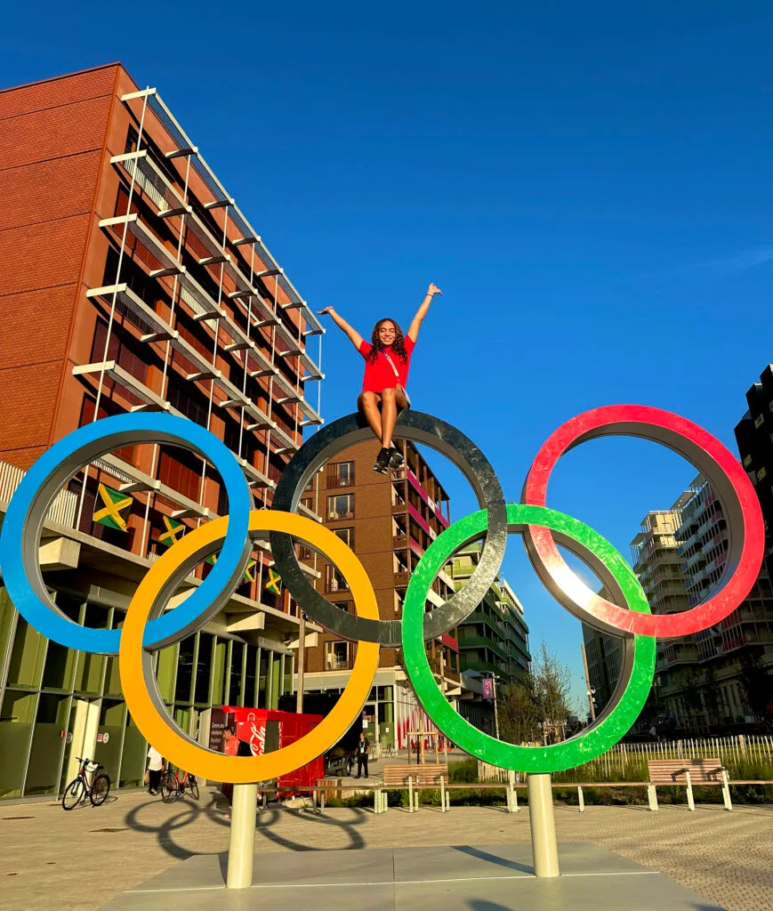Malak Tawfik sits high atop the interlocking Olympic rings structure, raising her arms in celebration.