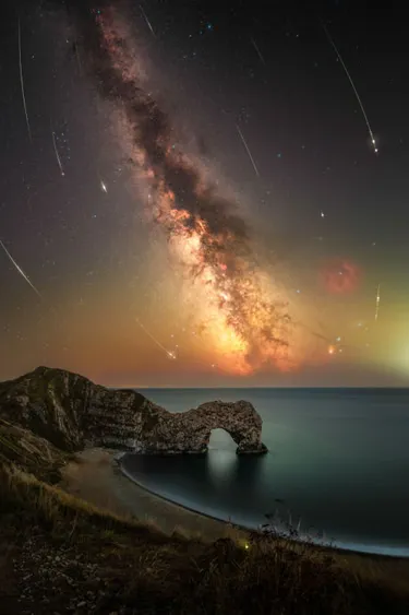 ‘Ancient fireworks’ from Comet Swift-Tuttle hurtled through the atmosphere with an ultra-wide angle lens the natural limestone arch of Durdle Door, Dorset, UK is included. In the foreground, a singular glow worm was documented amongst reeds along the sea cliff edge